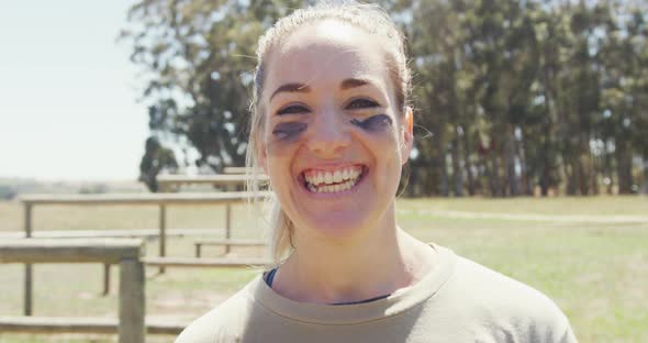Portrait of smiling female soldier wearing eye black standing in field on obstacle course in sun alt