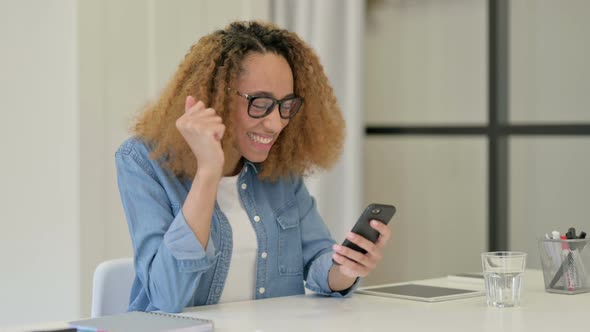 Successful African Woman Celebrating on Smartphone alt