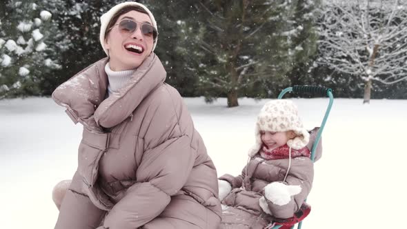 Young Happy Mother and Her Daughter Enjoying a Sledge Ride in a Beautiful Snowy Backyard alt