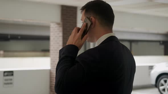 Businessman in a Black Suit Talking on the Phone in the Car Park alt