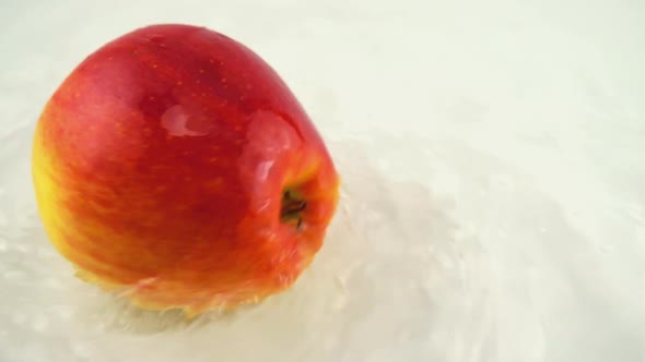 Rotating ripe apple in water on a white background. Slow motion. alt