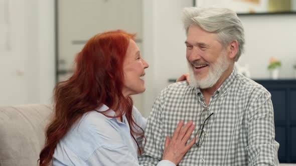 Loving Senior Couple Aged 6070 Hugging and Laughing While Sitting on the Couch at Home alt