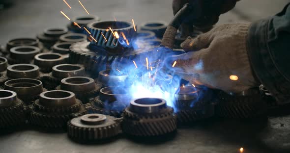 Welder Welds Metal Gears in One Decorative Detail at Workshop Welding and Metalwork at Locksmith's alt