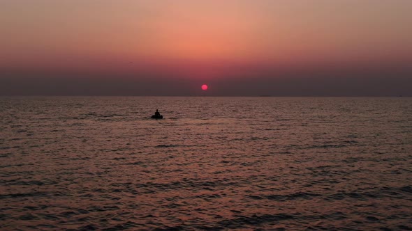 Drone flying around the lonely boat with a fishing man at sunrise in the sea.
