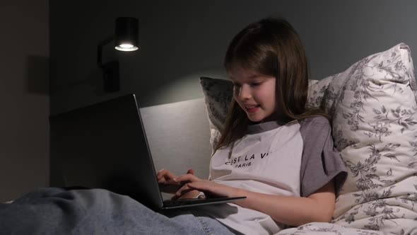 Little Girl Sitting with a Laptop at Night Playing Games Online Learning