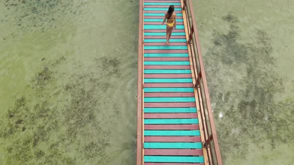 Sexy Brunette Woman in Yellow Bikini Walking on Wooden Bridge alt