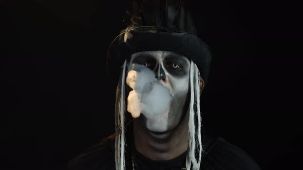 Sinister Man with Halloween Skeleton Makeup Exhaling Cigarette Smoking From His Mouth and Smiling alt