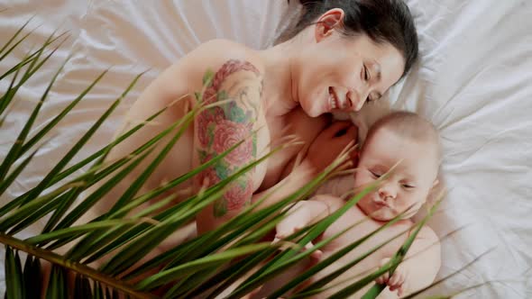 Loving Asian Young Mommy Hugging Soothing Adorable Sweet Baby Boy Lying in Bed alt