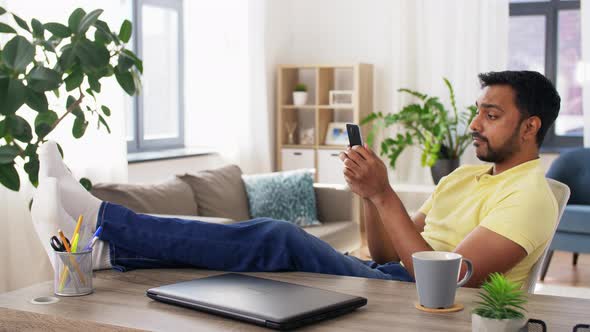 Indian Man with Smartphone Resting Feet on Table alt