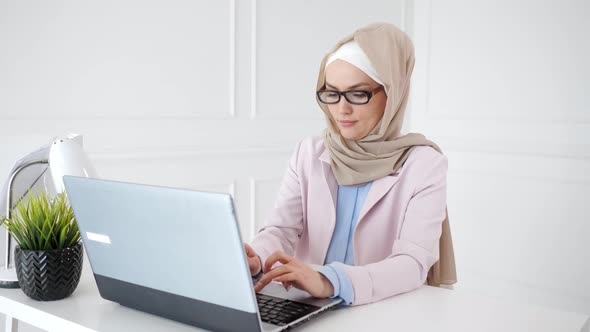 Beautiful Young Muslim Woman is Working on Laptop on Her Workplace alt