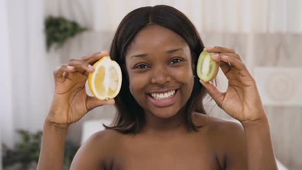Pretty Young African Woman Holding Kiwi and Lemon Slices in Hands alt