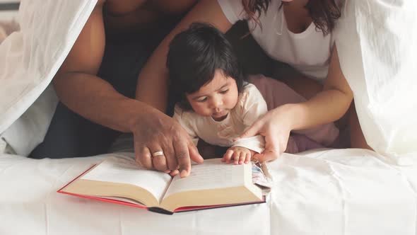 Multi-racial Family in Bedroom Under Blanket Reads a Children's Encyclopedia alt