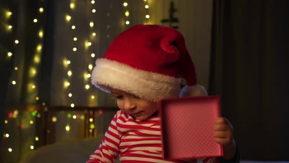 Christmas Boy Sitting in Santa Hat at Home Evening alt