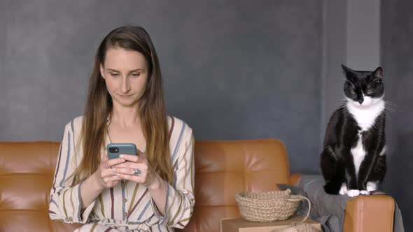 Woman Holding a Smartphone sitting on the Couch with her Cat and Working from Home, Copy Space alt