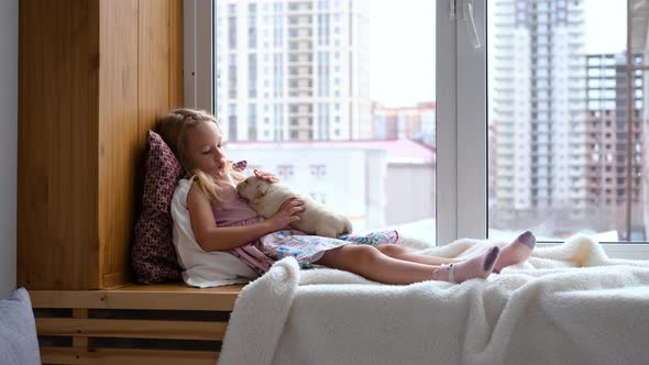 Little Girl Sitting on Windowsill with Puppy alt