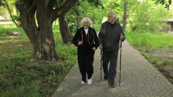 Active Senior Old Couple. Man Training Nordic Walking, Woman Running in Park alt