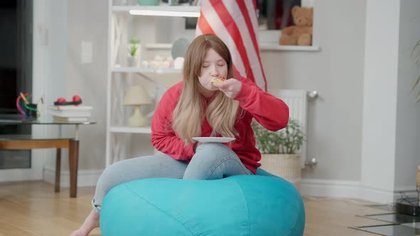 Relaxed Korean Teen Girl Watching TV and Eating Pizza Sitting on Bag Chair Indoors alt