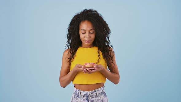 Young Darkskinned Woman in Casual Clothes is Holding a Donut Looking at It Licking Her Lips and alt