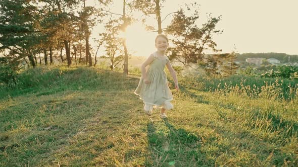 Cute Little Girl in a Green Summer Dress Runs Across the Lawn Smiling and Showing Her Tongue