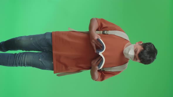 Asian Boy Student Wearing A Mask, Reading A Book While Walking On Green Screen alt