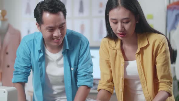 Asian Male And Female Designers Helping Each Other Rearrange The Papers While Designing Clothes alt