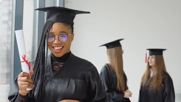 A Joyful Graduate with a Diploma in Hand Stands at the University Against the Background of alt