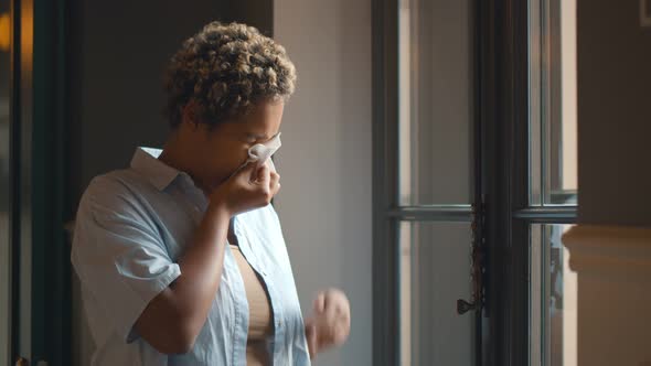 African Female Standing Near Window and Sneezing in Paper Tissue Having Pollen Allergy alt