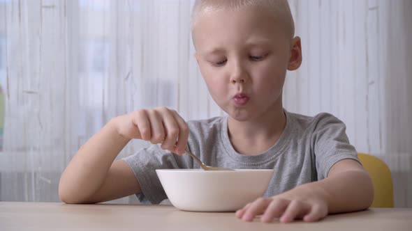 Cute satisfied little boy eating cereal with milk for breakfast. alt