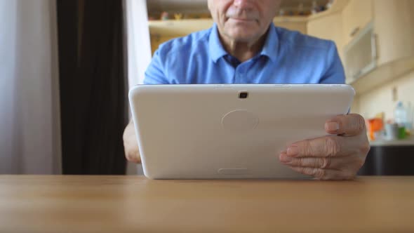 Aged Male Hands Types On A White Tablet Pc On A Table At Home