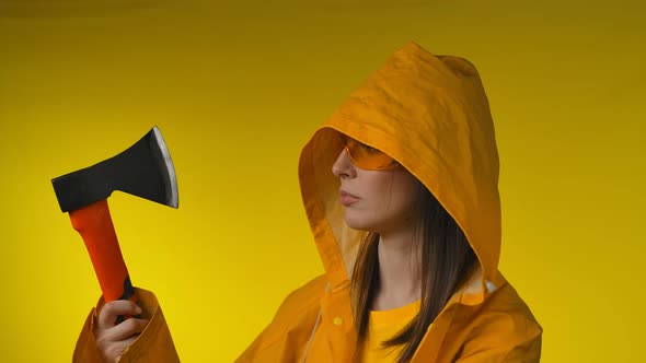 Young Beautiful Woman in a Yellow Raincoat is Checking an Axe in Her Hand alt