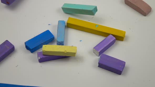 Sticks of multicolored chalks fall on a white background, slow motion alt
