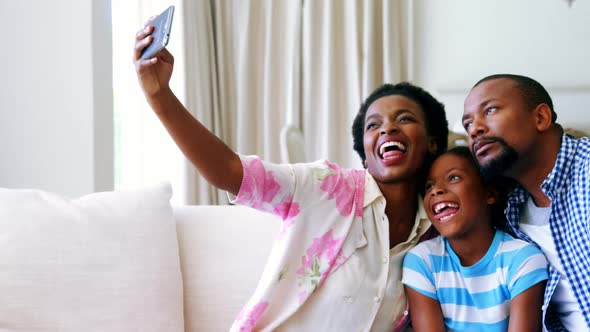 Family taking selfie on mobile phone in living room alt