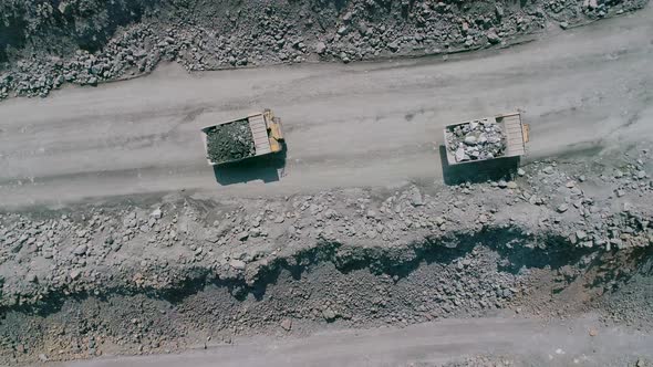 Mining Dump Trucks in Large Granite Open Pit Mine. Loaded Trucks Rides on Road Quarry Ledge Drone alt