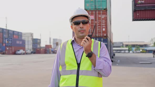 Engineer foreman talking on walkie-talkie with colleague in container warehouse alt