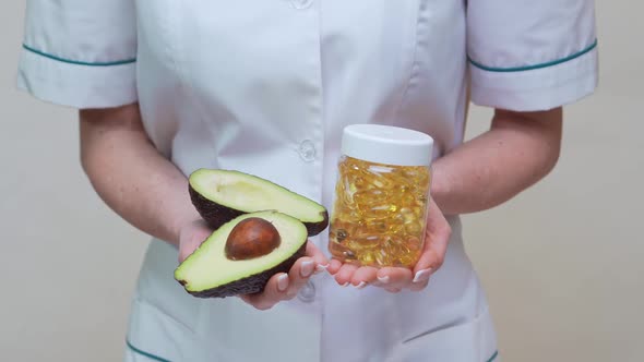 Nutritionist Doctor Holding Organic Avocado Fruit and Jar of Medicine or Vitamin or Omega 3 Capsules alt