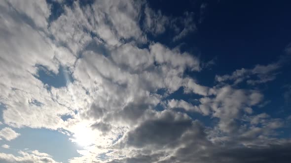 Time lapse: sun rays brake through fluffy clouds flying in the sky.