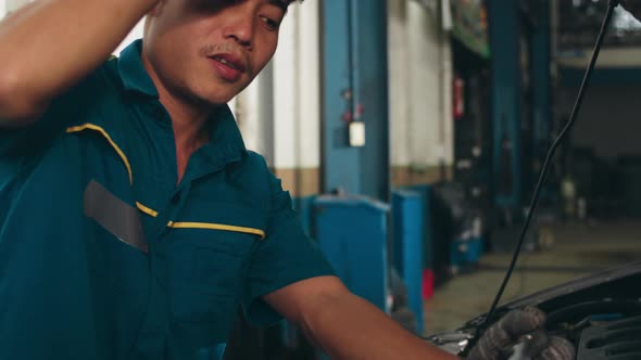 Skillful Asian guy in uniform fixing car at mechanics garage at night.