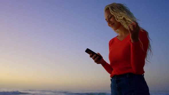 Woman using mobile phone on beach at dusk 