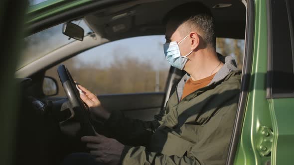 A Man in a Medical Mask Wipes the Steering Wheel in the Car with a Wet Cloth