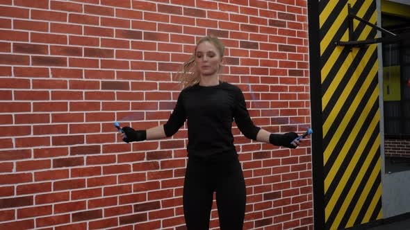 An Active Girl Jumps on a Rope in the Gym Against the Background of a Brick Wall alt
