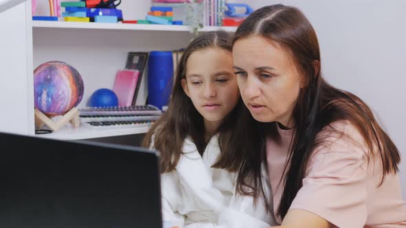 Mom Explains Homework to Her Daughter While Sitting in Front of a Laptop in the Nursery