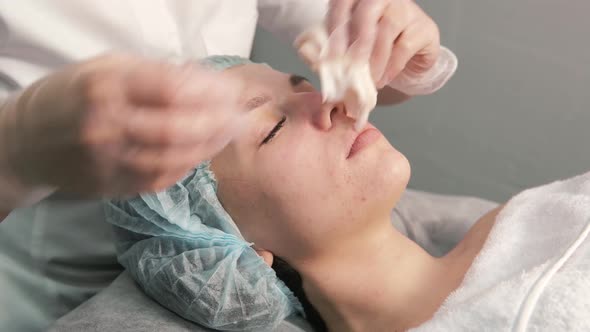 The Cosmetologist Cleans the Face of a Young Female Client with a Cloth Napkin