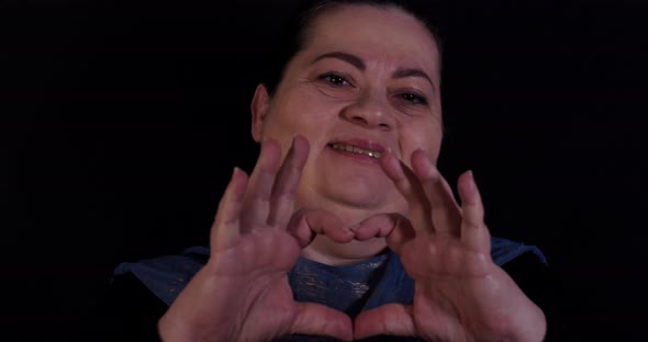 Middle aged woman holds her hands in heart shape