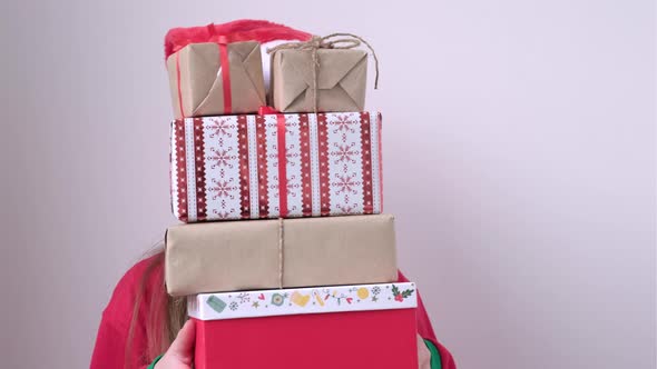 Smiling Little Girl Peeking Out From Behind a Pile of Gifts on White Background alt