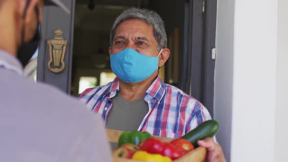 Senior mixed race man wearing face mask taking food delivery alt