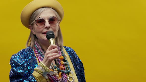 Portrait Of An Elderly Woman On Yellow Background With Microphone In His Hands alt