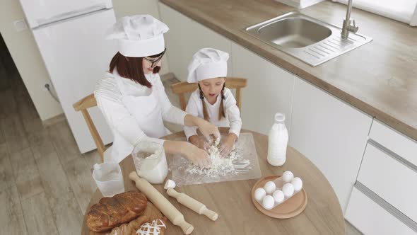 Happy Mother and Her Daughters in Hats of Chef and White Apron Making Dough for Baking alt