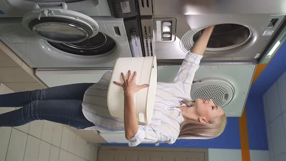 A Housewife Loads Laundry Into a Washing Machine in a Selfservice Laundry Room alt