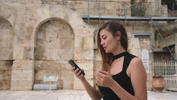 Brunette Traveler Woman with Phone for Chatting Inside of Acropolis in Greece alt