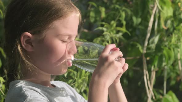 Kid Girl Drinking Water From Glass Outdoors on Green Background Side View alt